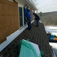 two men repairing a roof of a house