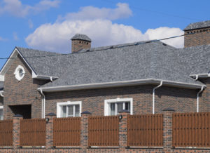 Asphalt shingle. Decorative bitumen shingles on the roof of a brick house. Fence made of corrugated metal.