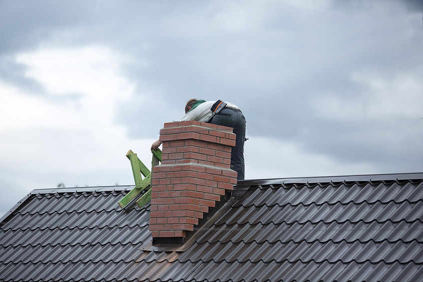 Worker on the roof repairs brick chimney