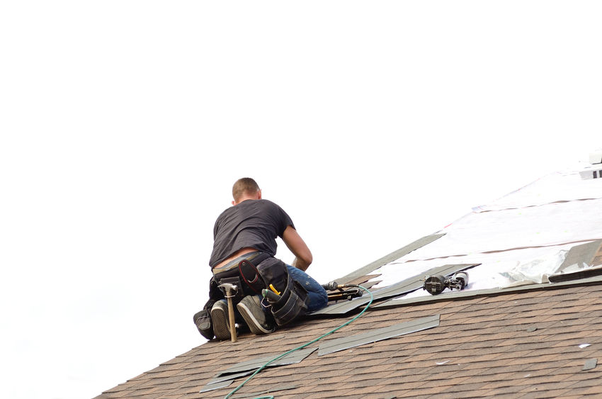 Roofer laying down asphalt roof shingles at a large commercial housing 