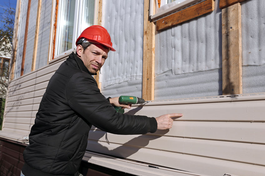 A worker installs panels beige siding on the facade of the house