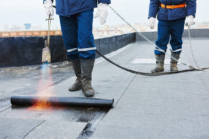 Flat roof installation. Heating and melting bitumen roofing felt by flame torch at construction site