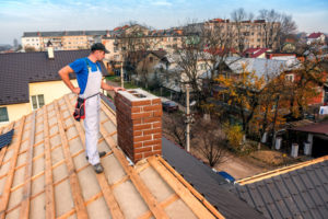 a professional master (roofer) with electric screwdriver covers repairs the roof near the chimney